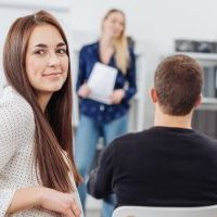 Young woman in a lecture or business presentation turning to smile at the camera viewed from the back of the room