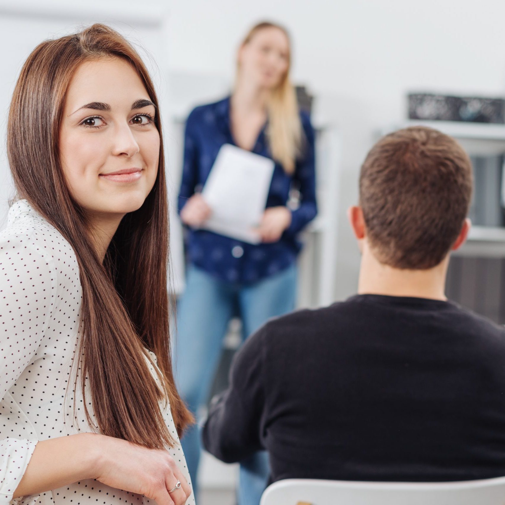 Young woman in a lecture or business presentation turning to smile at the camera viewed from the back of the room